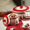 Christmas-themed cookie tins and plates with cookies and chocolates on a red tablecloth. Anteprima dell’immagine prodotto