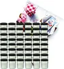 A set of glass jars with black lids, arranged in rows, with a decorative background featuring a checkered cloth, flowers, and a product package. Podgląd zdjęcia produktu