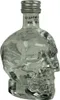 A clear glass bottle shaped like a skull, containing clear liquid, with a silver cap. Produktbild-Vorschau