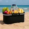 A picnic basket filled with groceries sits on a sandy beach with the ocean in the background. Anteprima dell’immagine prodotto