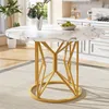 A round dining table with a marble-effect top and a geometric gold base is shown in a bright, modern kitchen or dining area. The table is set with a vase of flowers and a bowl of green apples. Náhľad obrázku produktu