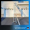 A tall, silver telescopic ladder is leaning against the side of a house with two garage doors. Náhľad obrázku produktu