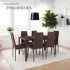 A dining room set with chairs and a table, set against a bright window and decorated with a large plant and wall art. Náhled obrázku produktu