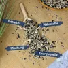 A wooden scoop filled with birdseed, scattered on a burlap surface, with labels pointing to different aspects of the seed mix. Produktbild-Vorschau