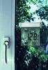 A digital window thermometer is attached to a window, showing temperature readings. The background is blurred greenery, suggesting an outdoor view. Náhľad obrázku produktu