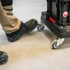 A person's foot is stepping on the wheel of a black transport cart. Náhled obrázku produktu