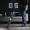 A person is vacuuming a living room floor with a cordless vacuum cleaner. Produktbild-Vorschau