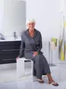 A woman is sitting on a white stool in a modern bathroom. Produktbild-Vorschau