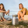 Two women sitting on a beach with a thermos bottle in the foreground. Náhled obrázku produktu