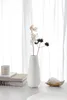 A white vase with dried flowers sits on a table in front of a white curtain. Produktbild-Vorschau