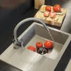 A kitchen sink with a faucet running water into it, and tomatoes on a cutting board in the background. Anteprima dell’immagine prodotto