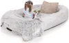 A young child and a small dog are sitting on a large, plush, light gray pet bed with a beige pillow. Produktbild-Vorschau