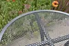 A close-up view of a round metal mesh table with a garden setting in the background. Produktbild-Vorschau