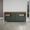 A dark green sideboard with a wooden top is shown in a room with light gray wooden plank walls and a light gray wooden floor. A window is visible on the right side. Podgląd zdjęcia produktu