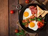 A full English breakfast is served in a cast iron pan on a wooden table. Produktbild-Vorschau