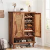 A wooden shoe cabinet with rattan doors, filled with shoes, is placed in a room with a lamp and a vase on top. Anteprima dell’immagine prodotto