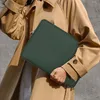 A person wearing a tan trench coat holds a dark green laptop sleeve. Anteprima dell’immagine prodotto