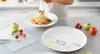 A person is serving pasta onto a plate, with other plates and tomatoes on a kitchen counter. Produktbild-Vorschau