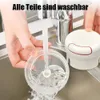 A person is rinsing a clear plastic food chopper with blades under a running faucet in a kitchen sink. A white and red food chopper lid is visible to the right. Produktbild-Vorschau