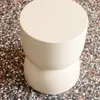 A close-up, top-down view of a cream-colored, hourglass-shaped side table on a speckled terrazzo floor. Anteprima dell’immagine prodotto