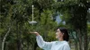 A woman is holding out her hand with a drone hovering above it in a natural outdoor setting with trees. Anteprima dell’immagine prodotto