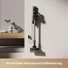 A cordless vacuum cleaner is mounted on a wall charging station next to a wooden console table with decorative items. Voir les images du produit