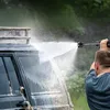 A person is pressure washing a muddy off-road vehicle. Produktbild-Vorschau
