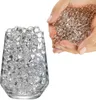 A hand holding clear water beads above a glass filled with the same beads. Produktbild-Vorschau