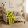 A cozy living room scene with a sofa, blanket, and side table. Produktbild-Vorschau