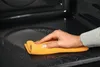 A hand is cleaning the inside of a dark appliance with a yellow cloth. Náhľad obrázku produktu