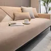 A close-up view of a sofa with a beige slipcover, featuring decorative pillows and a magazine on the seat. A coffee cup sits on a saucer. Produktbild-Vorschau