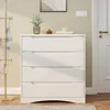 A white dresser with four drawers is shown in a room with a coat rack and a door. Náhled obrázku produktu