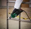 A person wearing black gloves is using a green and black electric grinder on a metal frame. Produktbild-Vorschau