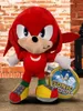 A plush toy of Knuckles the Echidna from Sonic the Hedgehog, standing next to a circular Sonic the Hedgehog branded item. Produktbild-Vorschau