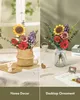 A split image showing a wooden flower bouquet in two different settings: one in a woven basket on a table, and the other in a glass vase on a desk with decorative items. Produktbild-Vorschau