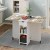 A folding kitchen table with storage shelves and a drawer, set up in a kitchen or dining area. Voir les images du produit