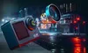 An action camera with its lens assembly exploded, set against a rainy, nighttime urban street scene with glowing lights. Anteprima dell’immagine prodotto