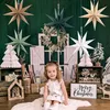 A young girl sits in front of a Christmas-themed backdrop with paper stars and trees. Produktbild-Vorschau
