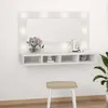 A white vanity mirror with LED lights and a shelf is mounted on a white wall above a stool. Produktbild-Vorschau