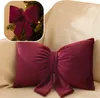 A decorative bow-shaped pillow on a sofa, with a smaller inset image of a similar bow on a Christmas tree. Produktbild-Vorschau