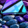 A close-up of a phone case with a gradient color effect, resting on a pile of colorful stones. Produktbild-Vorschau