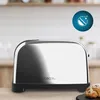 A shiny silver toaster sits on a wooden countertop, with a croissant in the foreground. Produktbild-Vorschau