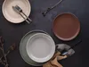 A flat lay of plates and cutlery on a dark surface, with decorative branches. Produktbild-Vorschau
