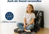 A young girl is sitting on a folded mat, which is leaning against a wall. The mat has a text pattern on it. Produktbild-Vorschau