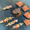 A variety of meats and vegetables are being grilled on a large, round, black grill surface. Produktbild-Vorschau
