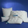 A white quilted duvet and pillows are arranged on a blue background. Produktbild-Vorschau