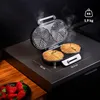 A waffle maker with two waffles cooking on a dark countertop, with strawberries in a bowl on the left. Produktbild-Vorschau