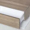 A close-up view of a wooden drawer with a white interior, part of a nightstand or shelf unit. Produktbild-Vorschau