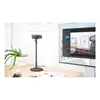 A desk setup with a webcam on a stand, a plant, a phone, and a large monitor displaying software. Produktbild-Vorschau