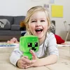 A young girl is lying on the floor, holding a green plush toy. Produktbild-Vorschau